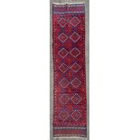 A hand-knotted Meshwani runner, central panel with repeating diamond and geometric motifs, red and