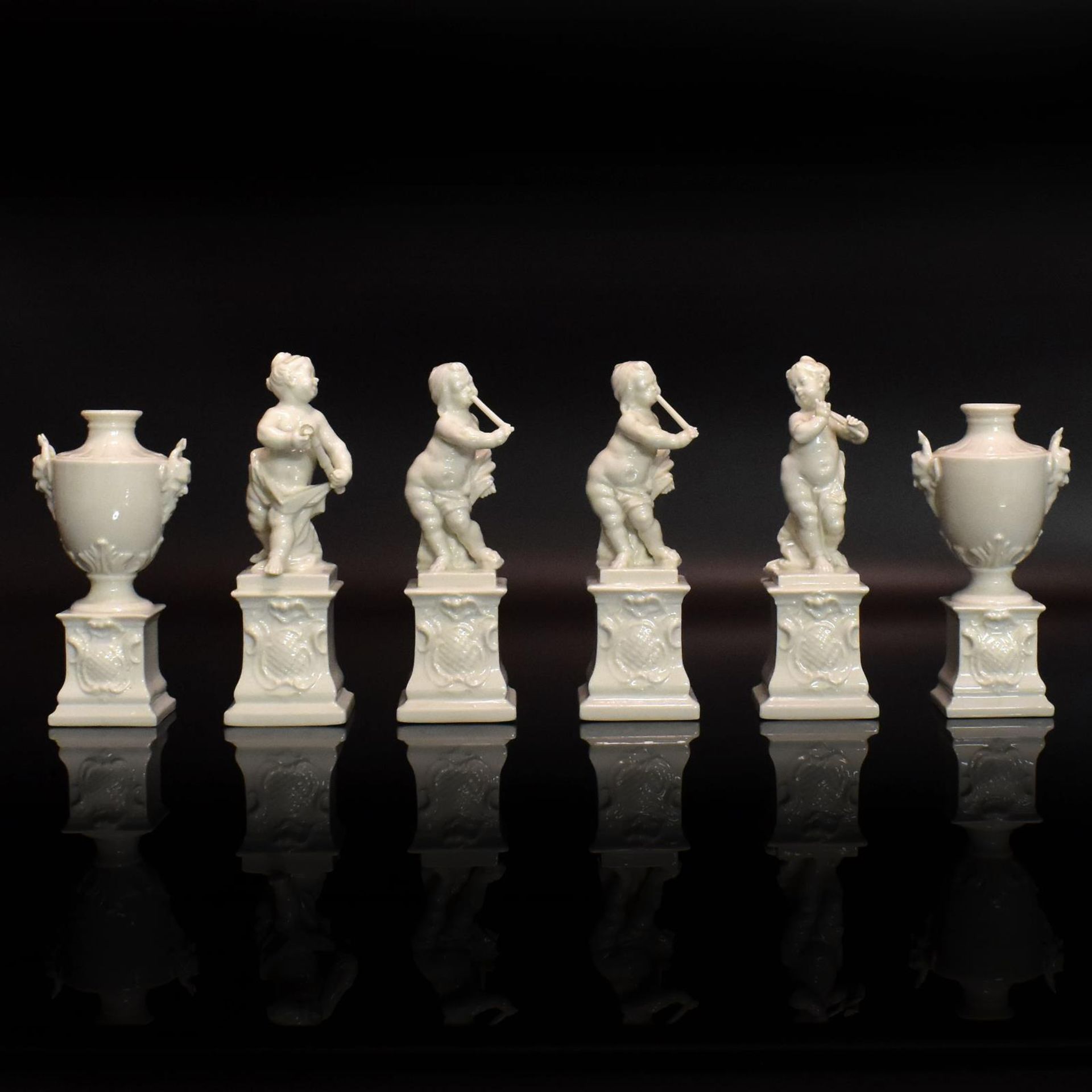 Vier Putten und zwei Ziervasen auf Postamenten. Nymphenburg | Porzellan, weiß.