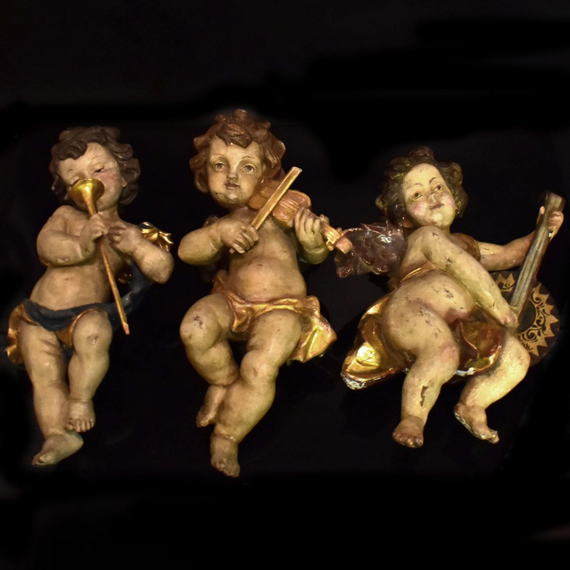 Drei musizierende Putten. Barockstil | Holz, geschnitzt, Farb- und Goldfassungen.