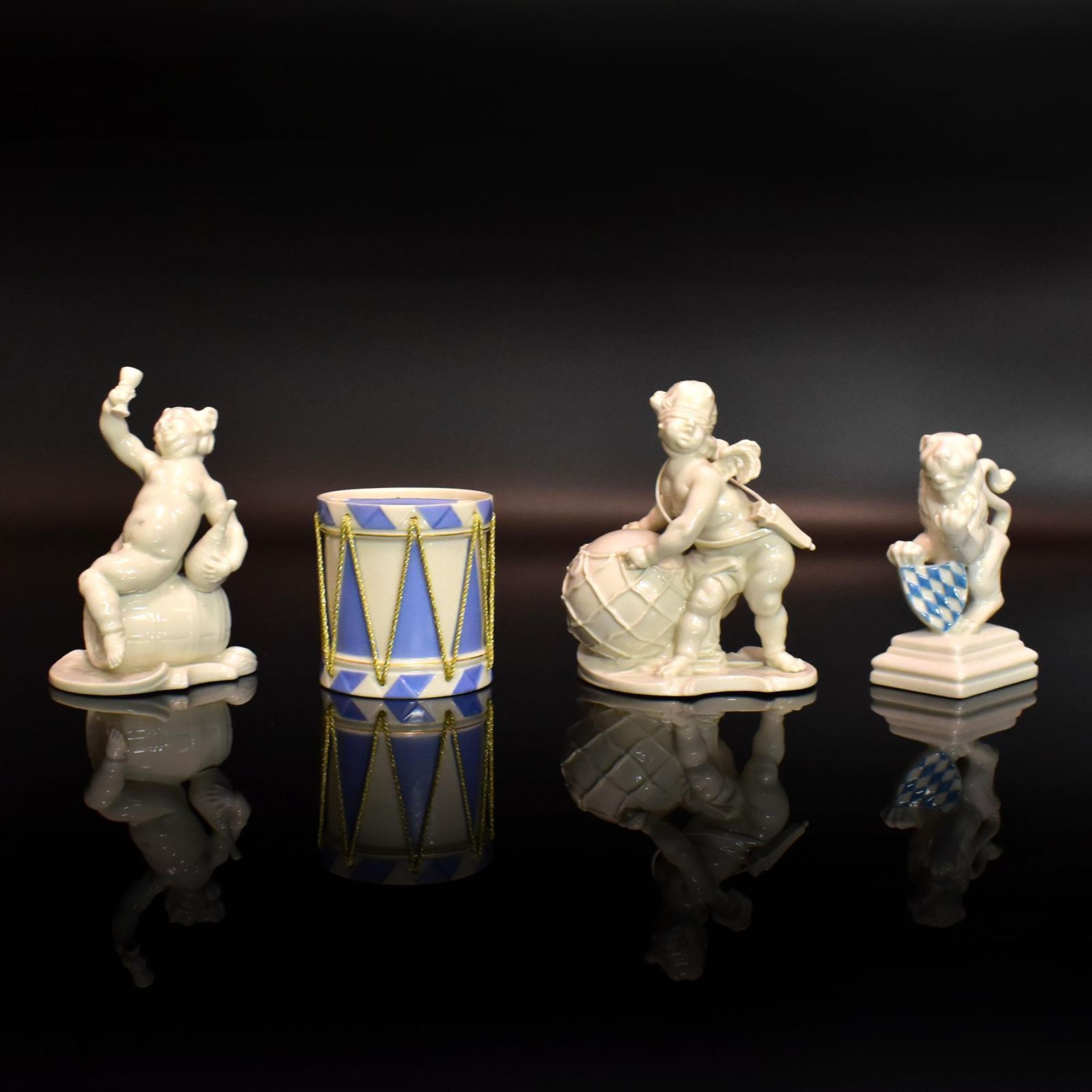 Zwei Putten, Wappenlöwe und Trommel. Nymphenburg | Porzellan, sparsam blau staffiert bzw. weiß.