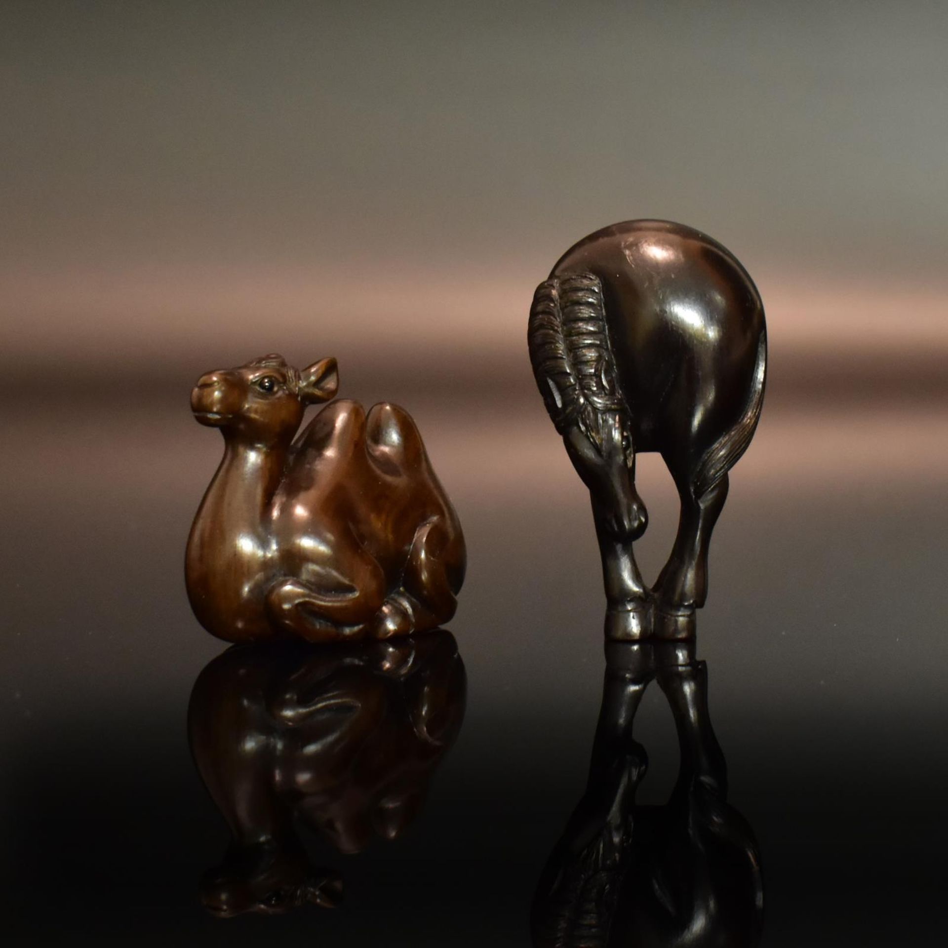 Zwei Netsuke: Grasendes Pferd / Liegendes Kamel. Japan, 19./20. Jh. | Buchsbaum, geschnitzt, Auge...