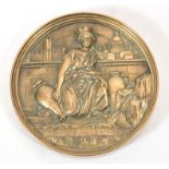 A brass medallion featuring a kneeling female form in high relief with a city scape in the