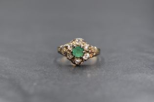 A yellow metal presumed gold emerald and diamond set cluster ring, the central emerald cut emerald