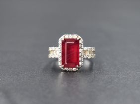 An 18ct white gold ruby and diamond set cluster ring, the central emerald cut ruby measuring appro