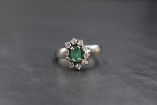 A white metal emerald and diamond cluster ring stamped 18ct having an oval emerald, approx 0.5ct