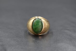 A yellow metal, presumed gold, gemstone set signet ring, the central oval green stone cabochon in