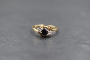 A 9ct gold sapphire and diamond three stone ring, the central round cut sapphire flanked by two