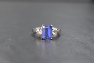 An 18ct white gold tanzanite and diamond three stone ring, the central emerald cut tanzanite measur