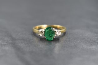 An 18ct gold emerald and diamond set three stone ring, the central oval cut emerald measuring