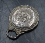 An Edwardian silver mounted hand mirror, having a decorative border with cherubs to the centre and a