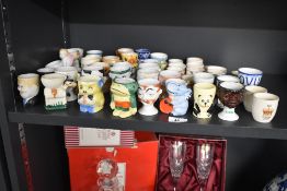A large selection of late 19th- to 20th-century ceramic novelty egg cups, some transferware and some