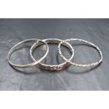 Three silver bangles, one of plain form, one having twist finish & the other having cut out knot