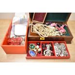 A wooden jewellery box along with a red plastic jewellery box, both containing an assortment of