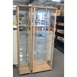 Two contemporary upright display cabinets, constructed with a light-toned wood frame, possibly
