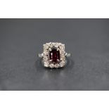 A platinum ruby and diamond set cluster ring, the central oval cut ruby measuring approximately 0.
