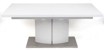 A modern white extending dining table, the rectangular top drawing out to reveal an additional extra