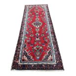 A hand-knotted Persian wool runner, the red field with a central floral medallion and scrolling