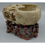 A Chinese jade cup with carved decoration and pierced handle upon carved hardwood stand, 12cms tall