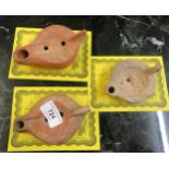 Two ancient Roman redware oil lamps, the largest 12cm long, together with another similar, each with