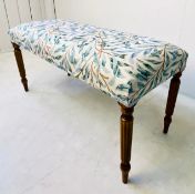 LONG STOOL WITH BOTANICAL DESIGN UPHOLSTERY ON REEDED SUPPORTS.