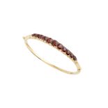 A late 19th century garnet bangle, the hinged bangle set to the front with a graduated row of oval-