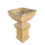 A large composition stone garden urn on stand, the square pot with moulded rim and floral embossed