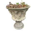 A composition stone garden urn with moulded rim above lobbed body embossed with masks floral fruit