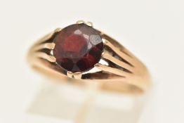A YELLOW METAL GARNET RING, gypsy set with a circular cut garnet, to a polished band, stamped 9ct,