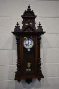 AN EARLY 20TH CENTURY WALL CLOCK, with three finials, the arched glass door enclosing a 6 inch brass