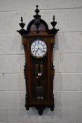 AN EARLY 20TH CENTURY WALNUT VIENNA WALL CLOCK, with three finials, the arched glass door
