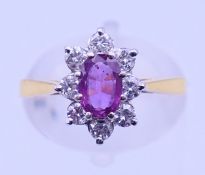 An 18 ct gold ruby ring, the oval cut stone surrounded by eight cut diamonds. Ring size M/N.