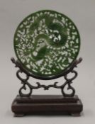A Chinese carved green stone roundel on a carved wooden stand. 23.5 cm high.