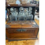 An Arts and Crafts oak three bottle tantalus, metal mounted, with three sherry glasses and three cut