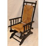 An ebonised American traditional rocking chair with seat and back upholstered in rush work on