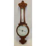 An old aneroid barometer with ceramic dial below thermometer in carved oak traditional case