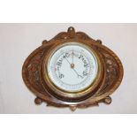 An aneroid barometer with circular dial and carved oak oval case