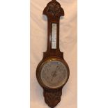 A good quality aneroid barometer with silvered circular dial below thermometer in carved oak
