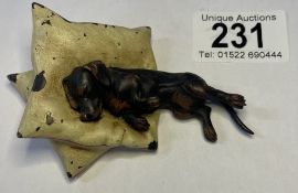 A cold painted bronze figure of a dog resting on two pillows