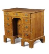 A GEORGE II ASH KNEEHOLE DESK C.1730 the quarter veneered and crossbanded top above an arrangement