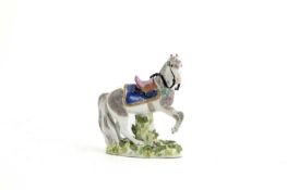A SMALL MEISSEN MODEL OF A PRANCING HORSE C.1750 with a blue saddle cloth and pink saddle, crossed