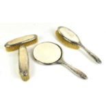 A four piece silver clad dressing table set, comprising a hand mirror, two clothes brushes and a